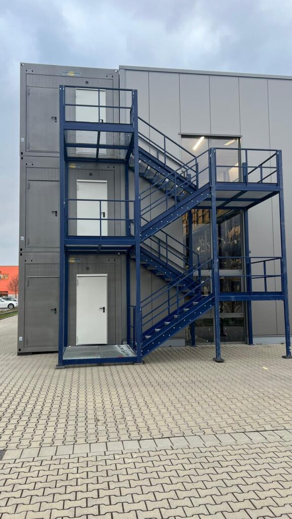 Ein Gerüst in blau, das auf der Vorderseite einer Containeranlage installiert ist.