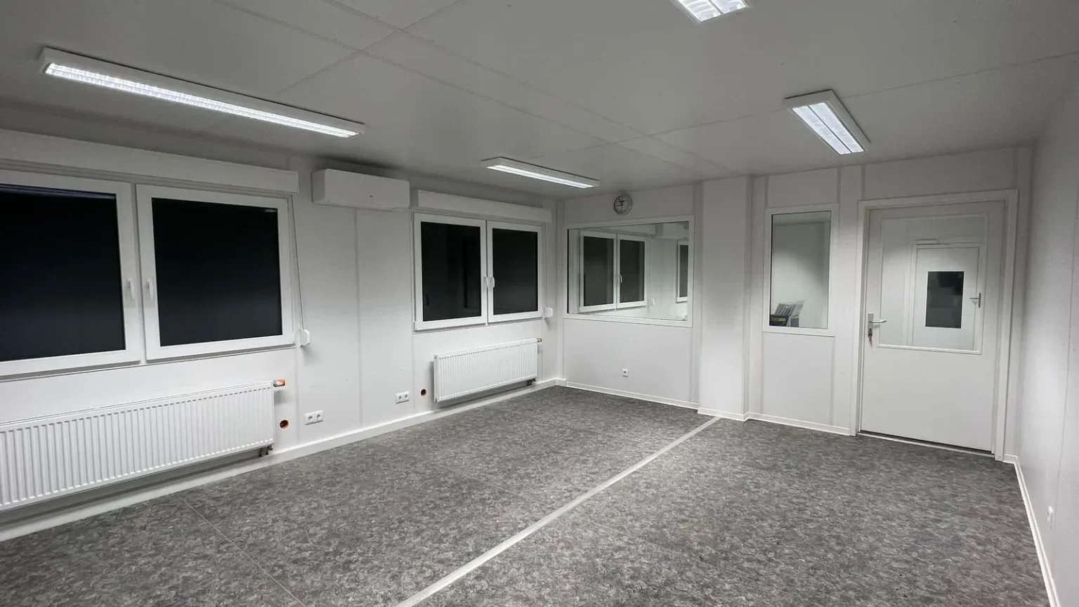 Immenraum eines Bürocontainer der Eurocontain GmbH. Mehrere Fenster an der linken Seite sind zu sehen, weiße Wände und ein grauer Boden sind vorhanden.